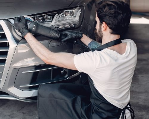 Man in a garage. Worker polish a car.